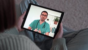 Young woman talking male doctor on tablet by video calling at home. Therapist beginning online consultation with client at videochat. People and psychology concept. Over shoulder view. 4k footage