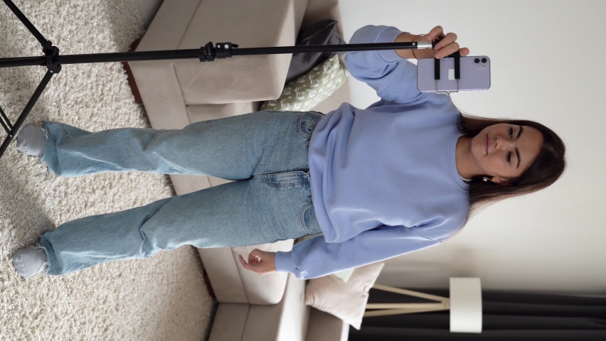 Vertical shoot. Happy young teenage girl in cornflower blue sweater dancing at home having fun listening to music enjoying weekend celebration with funky dance moves. 4k footage