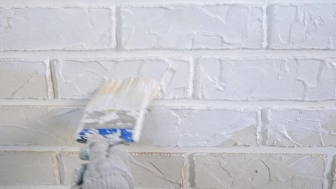 The master's hand paints a wall of decorative bricks with a brush with white paint with his own hands made of plaster. Repair the house yourself. Slow-motion close-up