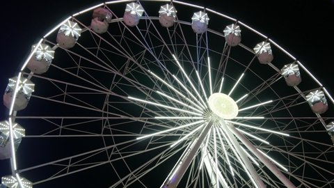 White big ferris wheel rotates against the background of the night sky. Ferris wheel with night illumination. lluminated Ferris Wheel construction