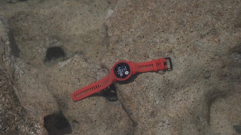 May 20, 2021 Cyprus, pathos. Sports watch with navigation and heart rate monitor garmin instinct flame red in clear sea water on rock. Smart watch theme for navigation, GPS positioning and tracking