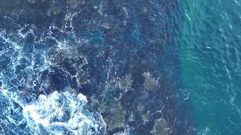 Waves and rocks. Sea waves texture. Nature background view from drone. Blue ocean water with rocks among foam. Water splashes with foam on the waves.