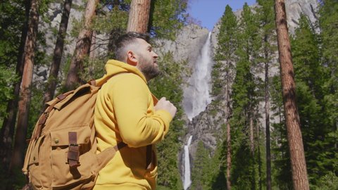 30s Forest Hiker Traveler Man in Woods Hiking in Yosemite National park with Waterfall View, Back Shot Concept. Contemporary Travel Guy with Tourist Backpack Standing in Nature Scenic, RED camera 6K