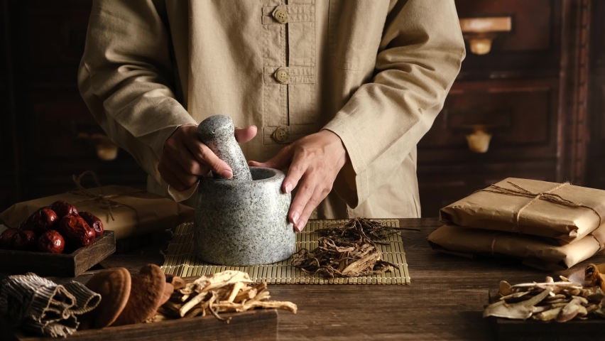 Front view of apocathery putting ingredient into mortar and pestle with chinese traditional medicine in wooden table  Royalty-Free Stock Footage #1089579703