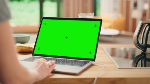 Close Up Green Screen Mock Up on Laptop Computer. Device is Used on a Kitchen Table in a Modern Home. Person Uses Touch Pad for Scrolling the Web. Sunny Modern Home with Healthy Lifestyle Atmosphere.
