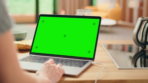 Close Up Green Screen Mock Up on a Laptop Computer. Device is Used on a Kitchen Table in a Modern Home. Person Uses Touch Pad for Scrolling the Web. Sunny Modern Kitchen with Healthy Lifestyle Vibes.