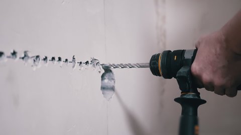 A Builder Using a Puncher Makes a Hole in a Concrete Wall to Install an Outlet. Rotation of a drill on an electric rotary hammer. Lots of flying cement dust. Installation of electrical wiring at home.