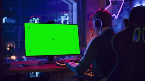 Excited Female Gamer Playing Online Video Game with a Mock Up Green Screen on Her Powerful Computer. Room and PC have Colorful Neon Led Lights. Cozy Evening at Home in Loft Apartment.