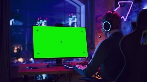 Concentrated Female Gamer Playing Online Video Game with a Mock Up Green Screen on Her Powerful Computer. Room and PC have Colorful Neon Led Lights. Cozy Evening at Home in Loft Apartment.