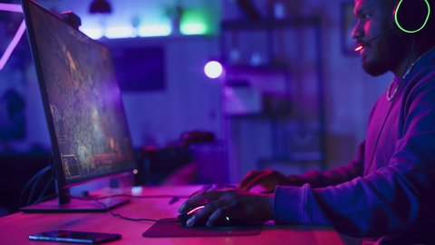 Excited Gamer Playing PRG Strategy Video Game in Which Players Fight in a Battle Royale Tournament on His Personal Computer. Room and PC with Neon Lights. Stylish Black Man in Cozy Room at Home.