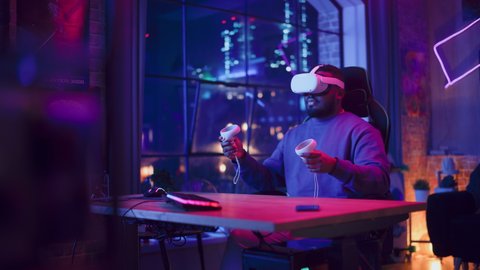 Young Man Using Virtual Reality Headset with Controllers at Home in Loft Apartment. Stylish Black Male Browsing Online, Spending Time in VR Software and Digital Office. POV from Screen Perspective.