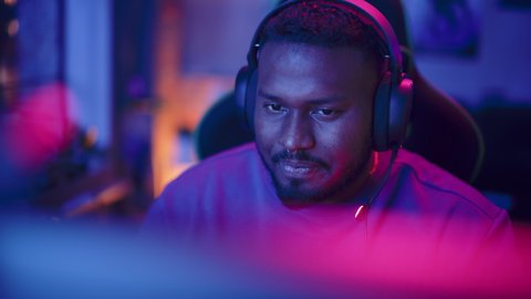 Successful Gamer Winning in Online Video Game on Computer. Close Up Portrait of Young Black Man in Headphones Playing PvP Tournament with Other Players, Talking with Team on Microphone.