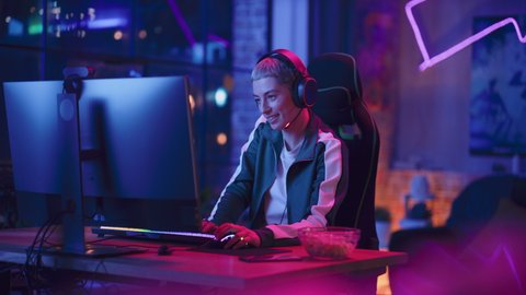 Portrait of a Female Gamer Playing Online Video Game on Computer. Stylish Young Woman with Short Hair in Headphones Enjoying Leisure Time, Smiling and Posing for Camera. Cyber Gaming Neon Room.