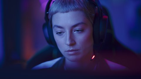 Portrait of a Female Gamer Playing Online Video Game on Computer. Close Up of Stylish Woman in Headphones Enjoying Leisure Time, Smiling and Posing for Camera. Cyber Gaming Stylish Retro Neon Room.