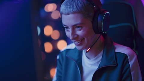 Excited Female Gamer Playing Online Video Game on Computer. Close Up Portrait of Young Stylish Woman in Headphones Battling in PvP Tournament with Other Players, Talking with Team on Microphone.