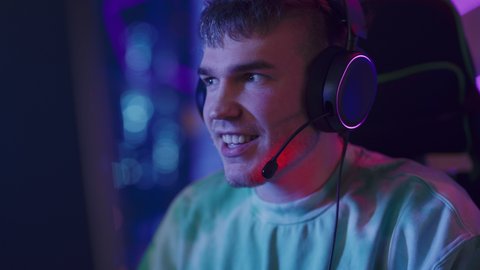 Gaming at Home: Gamer Playing Online Video Game on Computer. Close Up Portrait of Stylish Male in Headphones Enjoying Leisure Time, Talking with Players on Mic. Cyber Gaming Stylish Retro Neon Room.