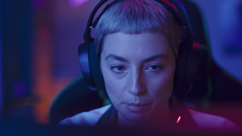 Portrait of a Female Gamer Playing Online Video Game on Computer. Close Up of Stylish Woman in Headphones Enjoying Leisure Time, Smiling and Posing for Camera. Cyber Gaming Stylish Retro Neon Room.