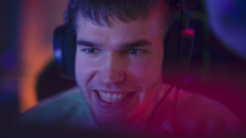 Professional Gamer Playing Online Video Game on Computer. Close Up Portrait of Stylish Male in Headphones Enjoying Leisure Time, Talking with Players on Mic. Cyber Gaming Stylish Retro Neon Room.