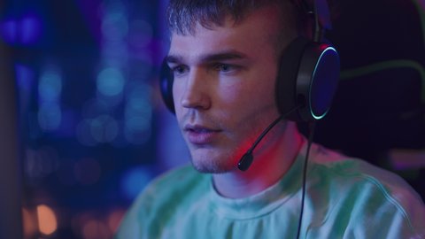 Portrait of a Gamer Playing Online Video Game on Computer. Close Up of Stylish Male in Headphones Enjoying Leisure Time, Smiling and Posing for Camera. Cyber Gaming Stylish Retro Neon Room.
