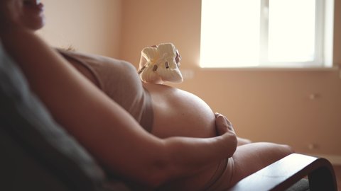 pregnant woman with belly. woman with big bare a belly holding booties baby shoes close-up indoor. health pregnancy motherhood procreation concept. girl preparing for motherhood