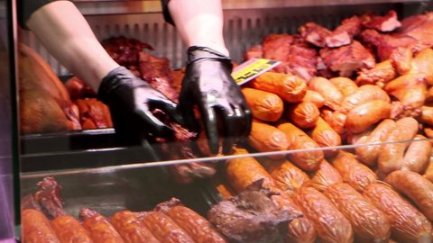 The salesman lays out smoked meat in the window display at grocery store. Close-up 4k footage
