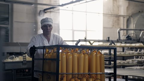 A breeder in a white uniform carries cheese in yellow packaging for further production. Delicious white cheese in large quantities is sent for further smoking. Modern dairy cheese plant. Dairy food