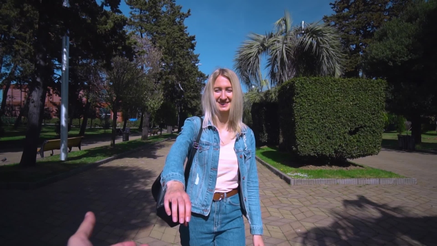 Shooting in first person, young beautiful blonde takes guy by hand and runs around city, through park on sunny day. woman in denim suit, girl. camera follows him. Travel enthusiasts. couple in love. Royalty-Free Stock Footage #1089585881