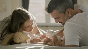 Loving young couple cuddling with their baby while having lazy weekend morning in bed. Happy long-haired woman tickling cute infant while child giggling. Dad smiling happily. Happy family concept - Powered by Shutterstock - Get 15% off with code: PIKWIZARD15
