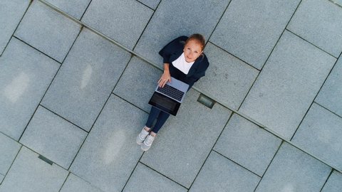 Big City Businesswoman Uses Laptop Computer During Lunch Break in Concrete Urban Park. Manager Goes Through Commercial and Financial Projects. Top-Down Zoom Out Aerial Drone Shot.