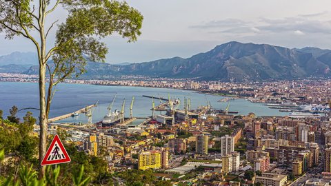 Static view of Foro Italico in Palermo, Sicily, Italy with view of a harbour busy loading ships in the evening in a timelapse.