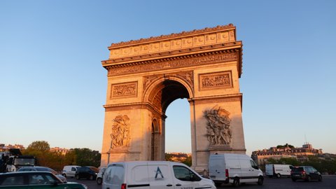 Paris France: Triumphal Arch of the Star (Arc de Triomphe de l'Étoile) - famous landmark and tourist attraction at sunrise. Traffic on the street in a sunny morning under clear blue sky. Apr 22.2022.