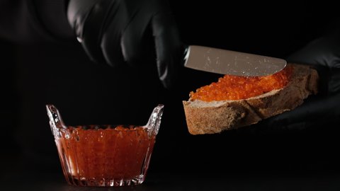 Spreads red caviar on bread with knife. Chef smears salmon caviar on toast. Close-up of knife is spreading caviar on bread. 