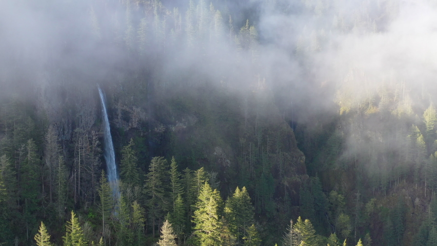 Mist drifts over a scenic waterfall plunging over 500 feet into the Columbia River Gorge, Oregon. This narrow canyon, with the Columbia River flowing through it, separates Oregon and Washington.