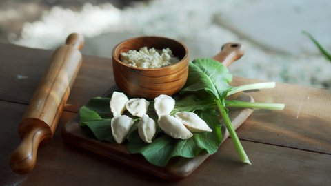 Traditional rustic Russian fresh handmade dumplings lying on a wooden table on a cutting board with cottage cheese in a wooden plate and spinach