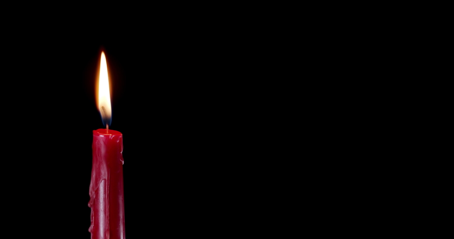 A single red candle burning. Isolated candle burning with dark background. Red paraffin candle with yellow shades burns on a black background. Background or illustration of remembrance or celebration. Royalty-Free Stock Footage #1089596987