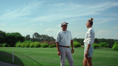 Two golfers talking sport on course. Golf players chatting on fairway grass. Smiling business partners standing on golfing field. Relaxed couple enjoy discussing game. Wealthy lifestyle hobby concept.