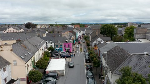 Forwards fly above narrowing street in town centre. Shops and services in houses along street. Ennis, Ireland