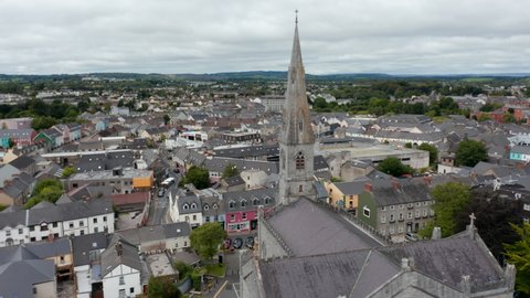 Fly around tall spire of Catholic cathedral. Aerial view of town development. Buildings and streets in town centre. Ennis, Ireland