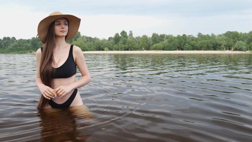 A young girl in a black bathing suit walks in the dark water. Portrait of a girl with long hair swims. slow motion