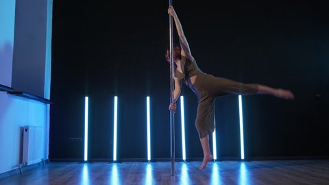 Slim girl near dance pole. Pretty woman doing poledance in studio. Exotic dance at blue light background. Exotic dance. Young woman performing sensual pole dance. 4K, UHD