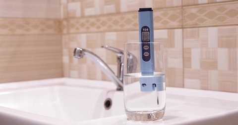 Measurement of TDS of water. Electronic pH meter in a glass of water. In the background is a tap for drinking water. Cleaning the water in the bathroom.