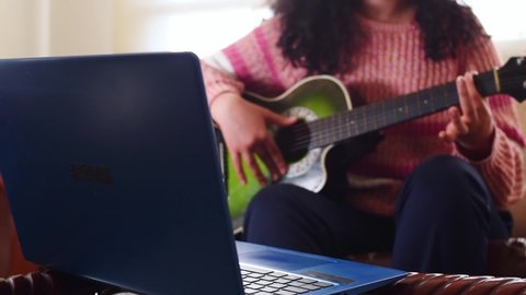 Teen learning to play guitar with a laptop