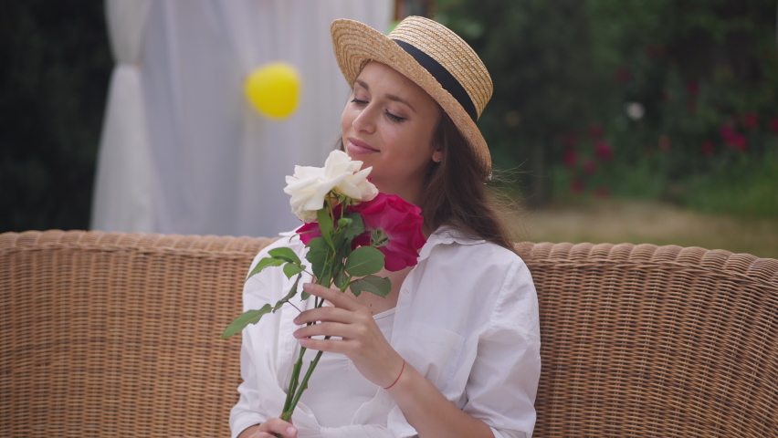 Front view zoom in of beautiful slim Caucasian young woman smelling bouquet of roses smiling looking at camera. Portrait of gorgeous confident brunette millennial with brown eyes posing with flowers