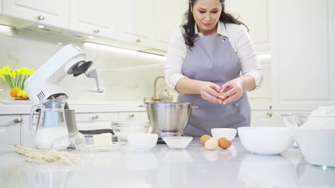 A woman cook breaks an egg and separates yolks from proteins to prepare cream or dough in a mixer bowl. cooking courses and dessert recipes. family business. online lessons for cooks.