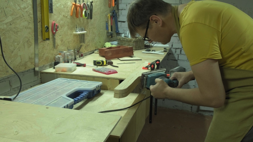 A mature carpenter makes a shelf in his carpentry workshop, works with a tool with wood 4k