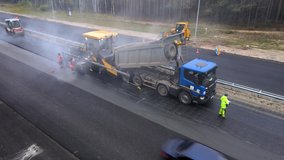 A paver coupled to a truck moves slowly down the track. The roller levels the hot paved asphalt. Road signs indicate the repair area. Workers in bright overalls laying new asphalt on the forest road. - Powered by Shutterstock - Get 15% off with code: PIKWIZARD15