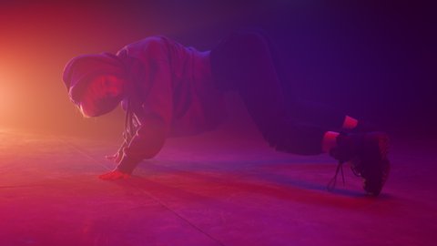 Dancer woman twerking on floor night club close up. Attractive blonde moving body seductive in studio neon lights. Sexy girl performing booty dance wearing hoodie in ultraviolet backlit indoors.