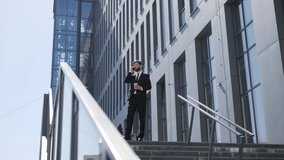 Portrait of confident successful businessman wearing formal suit with tie standing outdoors holding coffee, having business mobile phone call waiting for someone near office building, full length.
