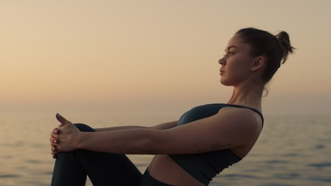 Strong sportswoman raise up leg holding knee by hands outdoors. Sporty woman stretching feet on beach summer evening. Focused slim girl making gymnastic exercises at dusk. Yoga fitness concept.