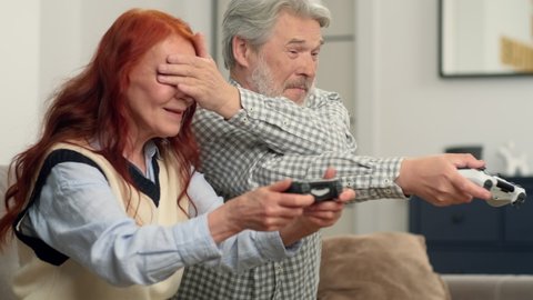 Cheerful senior couple 50-60 years old playing football using video game at home sitting on the couch. Game On, Family Meeting, Multi Ethnic Family, Different Generations.